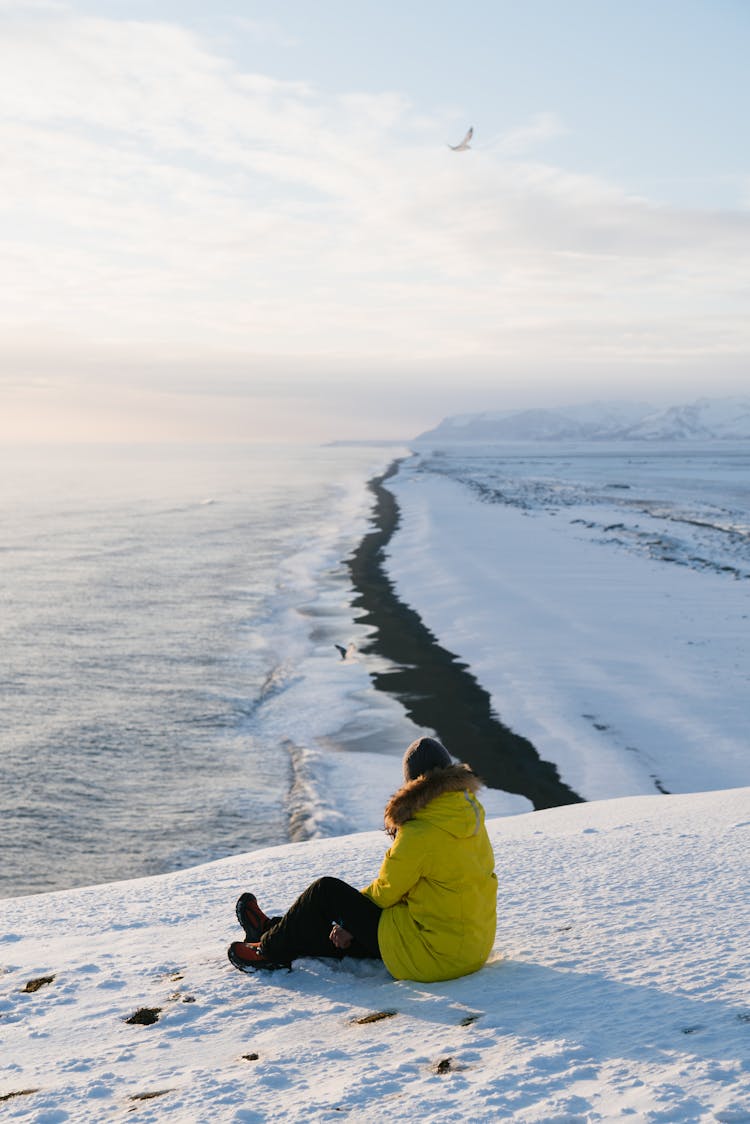 A Person Sitting On A Snow Covered Ground While Wearing A Yellow Parka