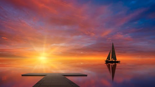 Wooden pier with sailboat in calm water at colorful sunset
