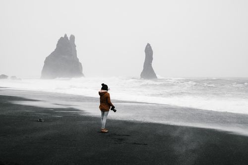 Free Photographer stands on a foggy beach with stunning black sands and rugged sea stacks. Stock Photo
