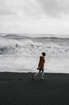 A photographer wanders along a stormy beach with waves crashing ashore, capturing nature's power.
