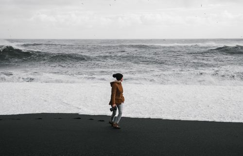 Free A woman strolls along the black sand beach with ocean waves crashing nearby. Stock Photo