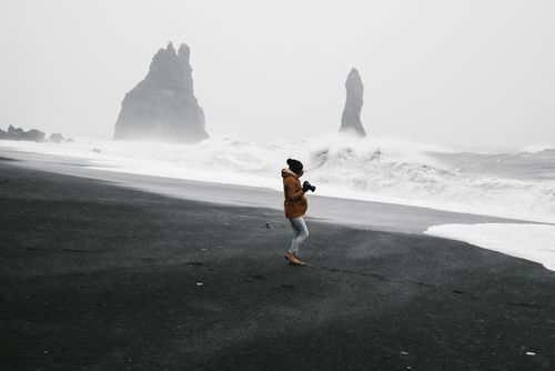 Free A photographer captures the dramatic waves and basalt sea stacks on a foggy day at Reynisfjara Beach. Stock Photo