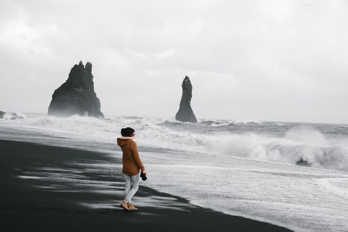 Free A lone photographer stands on Iceland's black sand beach with dramatic sea stacks and waves. Stock Photo