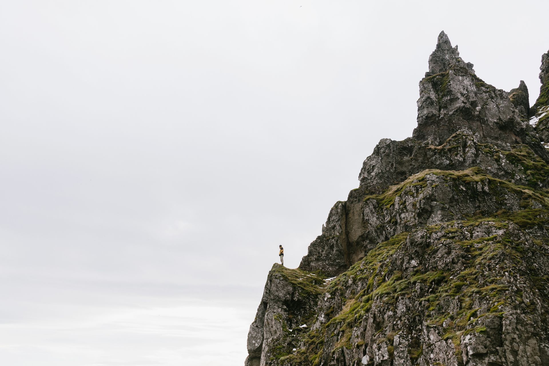 A lone figure atop a rugged mountain cliff under a cloudy sky, evoking adventure.