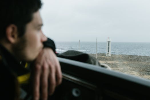 A man looking out at a lighthouse on a cloudy seaside day, evoking contemplation.