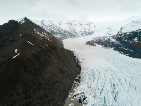 A stunning aerial view of a glacier framed by rugged mountains during winter.
