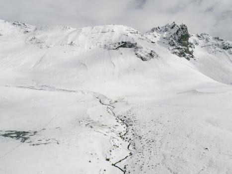 A serene aerial view of a snow-covered mountain landscape under a cloudy sky.