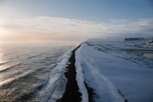 Free A breathtaking aerial view of a snowy coastline during sunrise, capturing the serene winter seascape. Stock Photo
