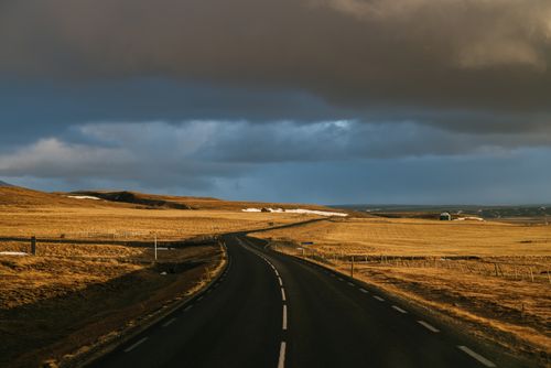 Free A winding highway through a rural landscape under dramatic autumn clouds, creating an atmospheric scene. Stock Photo