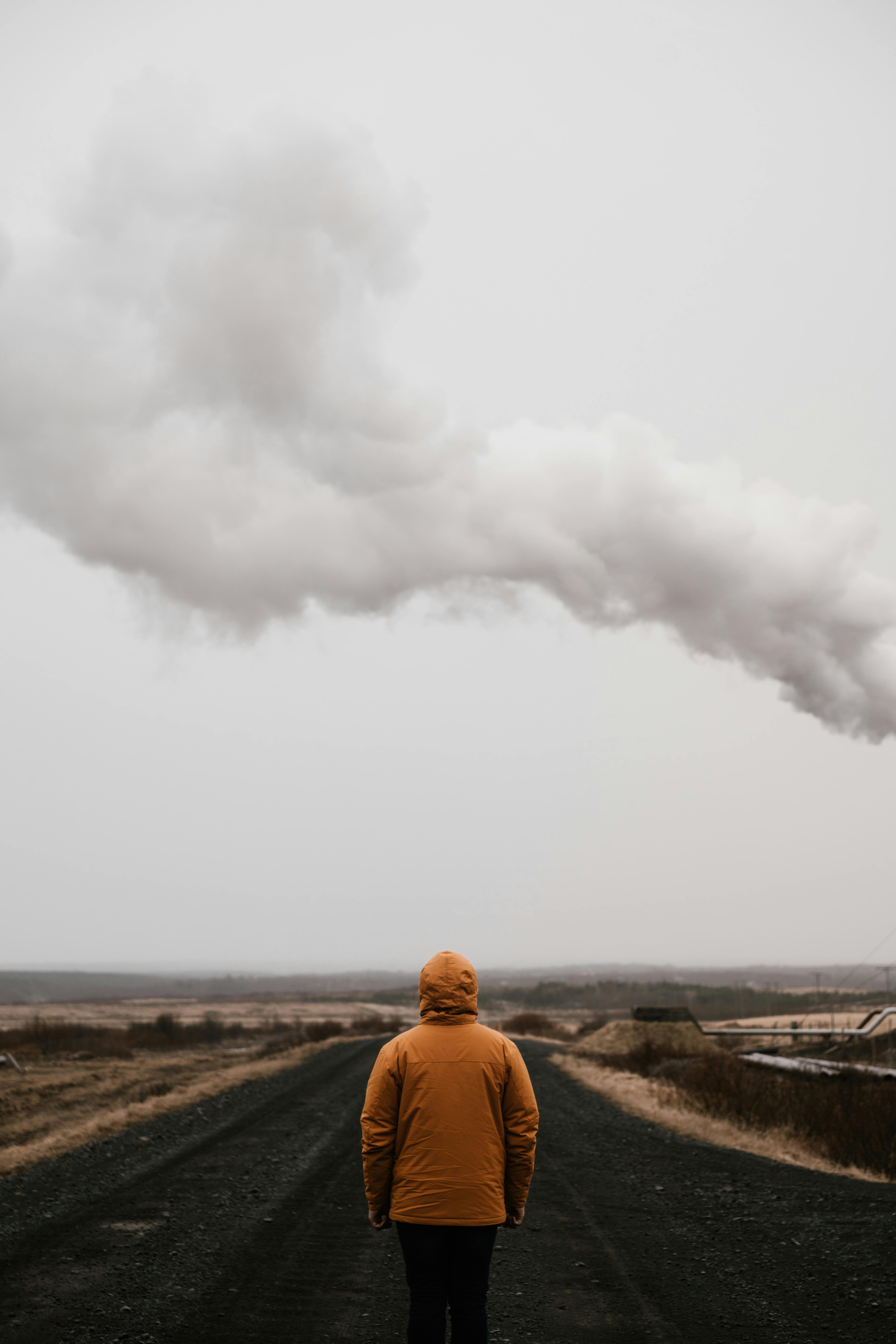 阴云密布的天空下，一个穿着黄色外套的孤独身影，站在荒凉的道路上，唤起一种隔离与沉思之感