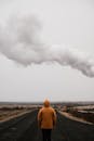 阴云密布的天空下，一个穿着黄色外套的孤独身影，站在荒凉的道路上，唤起一种隔离与沉思之感