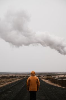 阴云密布的天空下，一个穿着黄色外套的孤独身影，站在荒凉的道路上，唤起一种隔离与沉思之感