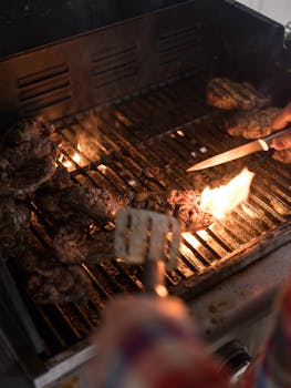 Close-up of juicy steaks being grilled with flames on a barbecue grill, capturing the essence of outdoor cooking.