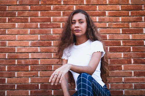 Stylish young lady sitting on haunches near brick building