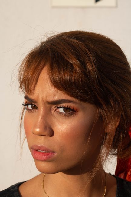 Dissatisfied young ethnic female with foxy hair standing near white wall on street and looking at camera with suspicion