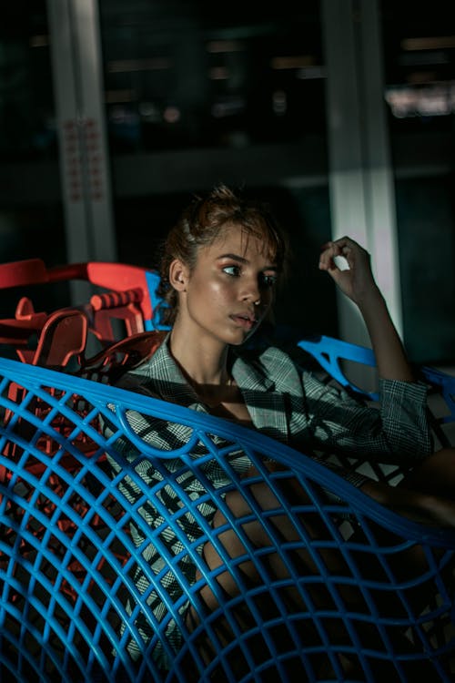 Free Thoughtful young woman sitting in supermarket cart Stock Photo