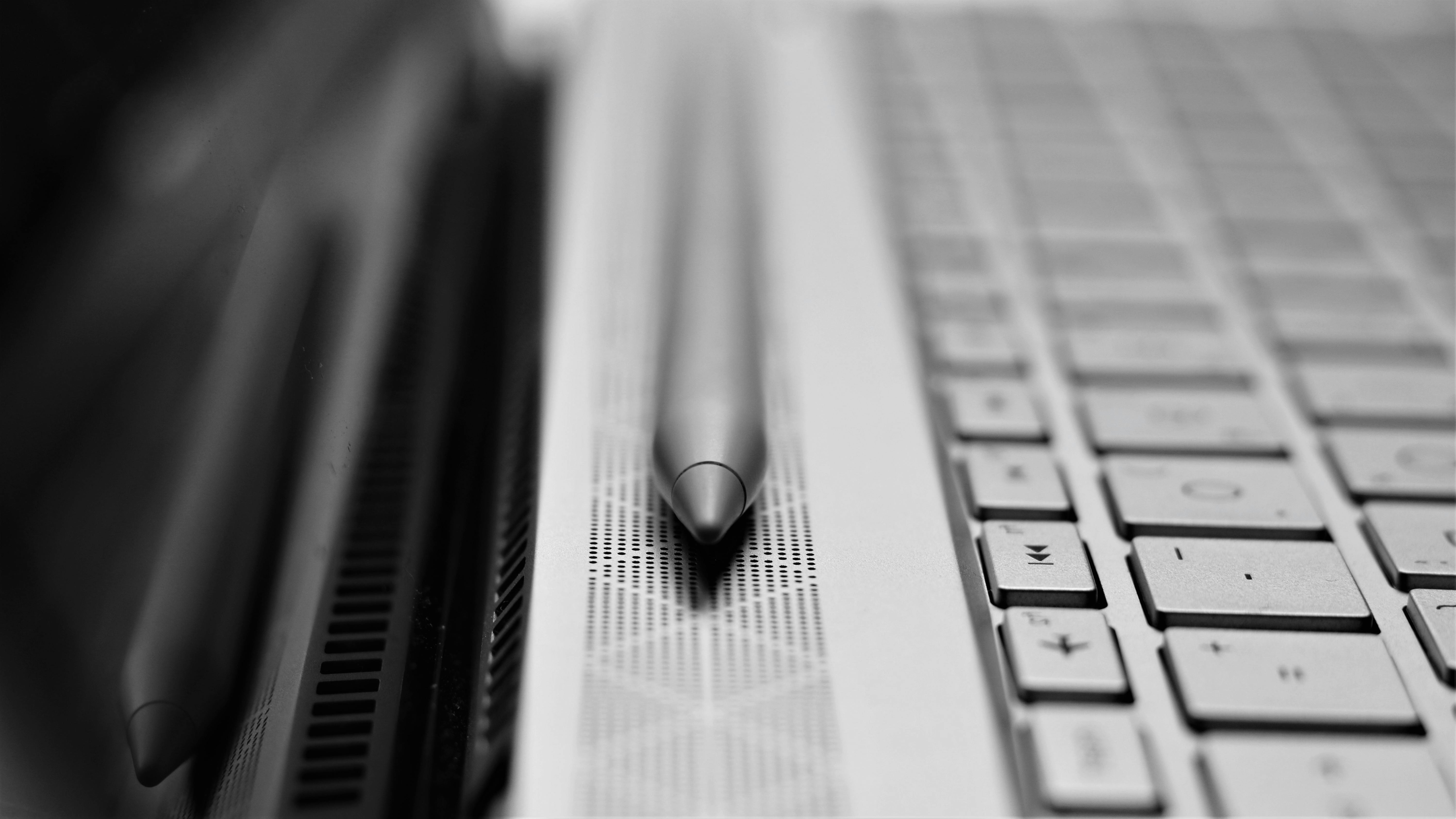 Black and white close-up of a stylus resting on a laptop keyboard, highlighting technology and design.