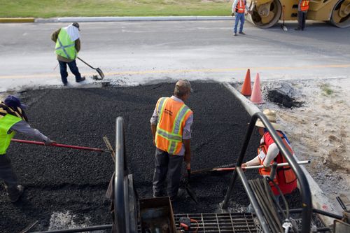 Free Group of road construction workers laying fresh asphalt outdoors during the day. Stock Photo