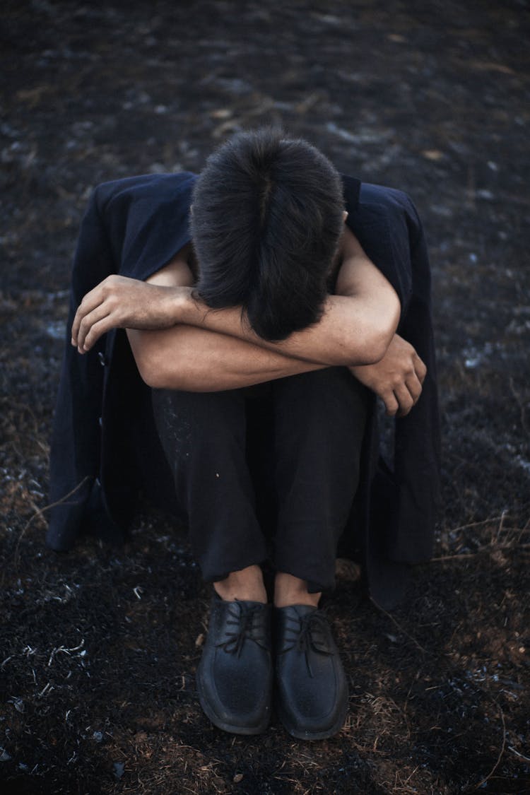 Unrecognizable Depressed Man Embracing Knees On Ground