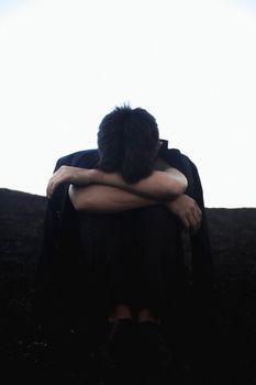 一名疲倦的年轻男子穿着便服坐在地上，抱着膝盖