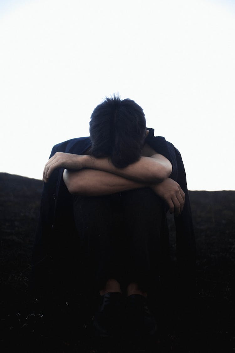 Unrecognizable Upset Man Sitting On Ground And Embracing Knees