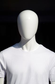 Close-up of a white mannequin wearing a white shirt against a black background.