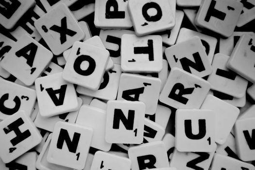 Grayscale close-up of Scrabble tiles creating a textured pattern of letters.