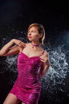 Young slim model wearing burlesque sequin dress standing in splashes of water on black background