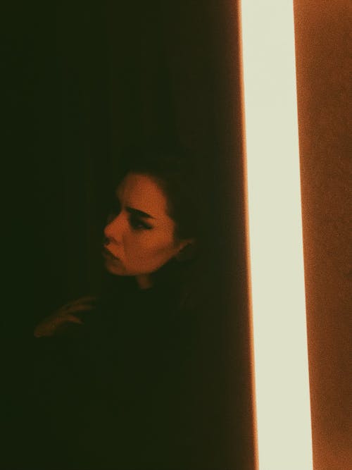 Free High angle of thoughtful female in reflection of mirror with bright lamp sitting alone in darkness Stock Photo