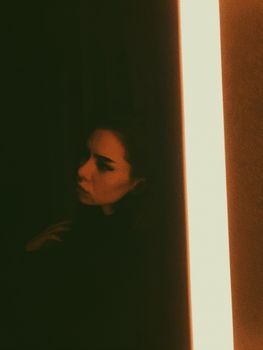 一位高挑而深思熟虑的女性，独自坐在黑暗中，身影映在镜子里，被明亮的灯光照亮