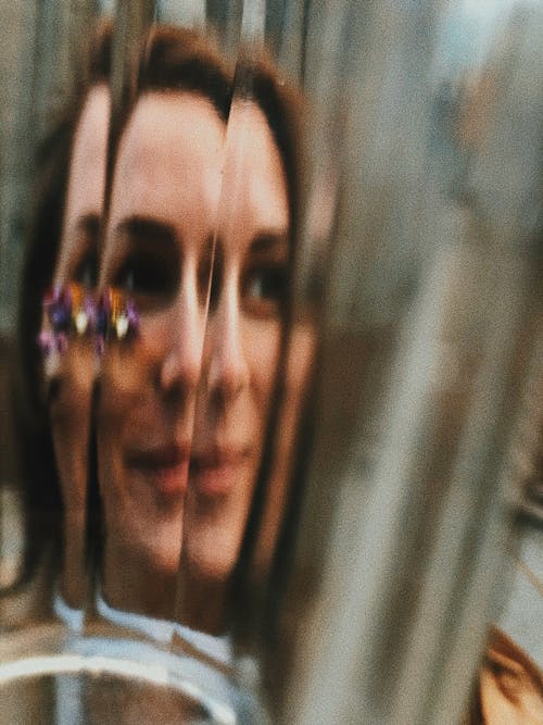 Through glass view of cheerful young female with floral decoration on face looking away
