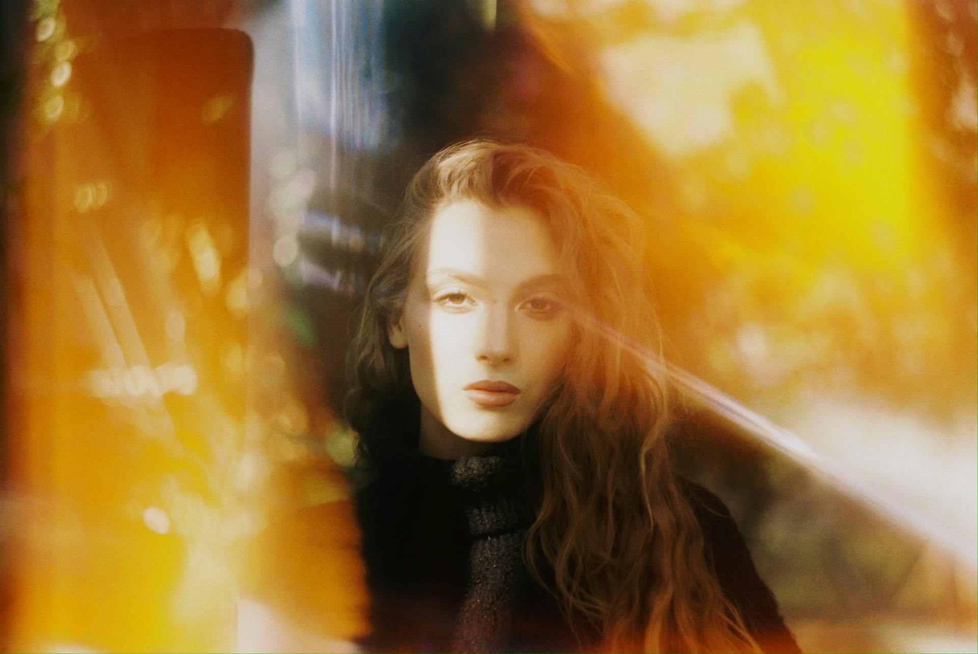 Young alluring female with long hair in bright yellow lights looking at camera