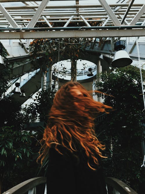 Young woman shaking head from side to side while standing among green plants in greenhouse
