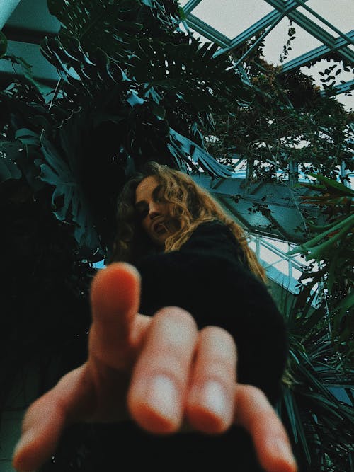 Woman pointing at camera standing in greenhouse