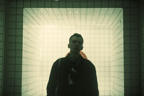 Free Stylish man in black jacket stands in a futuristic tiled corridor. Stock Photo