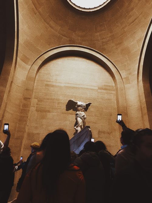 Free From below of crowd of people standing near Ancient Greek marble sculpture of goddess Nike and taking pictures Stock Photo