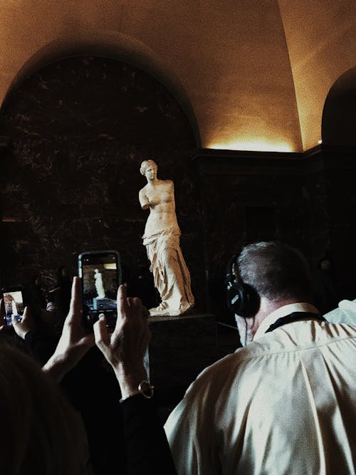 Travelers taking picture of Venus de Milo statue and listening audio guide while visiting historic sights
