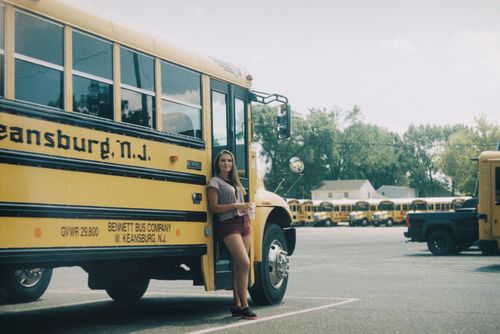 Free Full body of smiling female in summer clothes leaning on yellow bus on parking lot Stock Photo