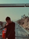 Young man with bag standing on bridge against fence