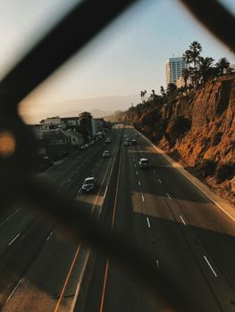From above of contemporary cars driving on smooth surface of roadway near hills and houses