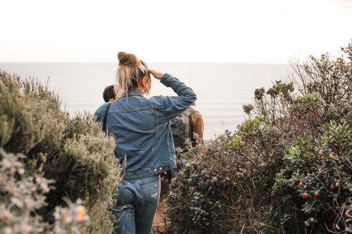 Free A woman in denim walks through a coastal pathway overlooking the sea, surrounded by nature. Stock Photo