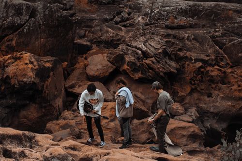Free Three young adults explore a rocky landscape, one holding a guitar, amidst an arid setting. Stock Photo