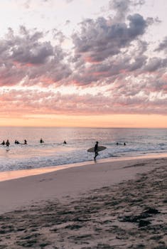 A tranquil beach scene with surfers and a colorful sunset sky, perfect for travel and lifestyle themes.