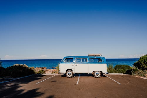 Vibrant blue cloudless sky over vintage trailer parked on asphalt next to coast blue endless ocean in sunlight