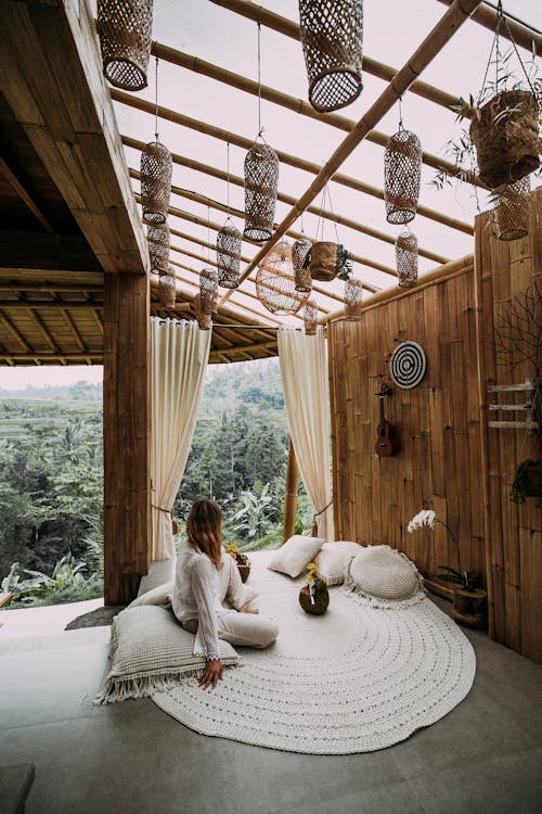 Faceless female relaxing on road carpet in big spacious gazebo decorated with pot plant and lanterns in valley immersed in green