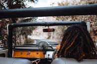 Back view of unrecognizable traveler with stylish dreadlocks spinning steering wheel while driving car and reflecting in small mirror