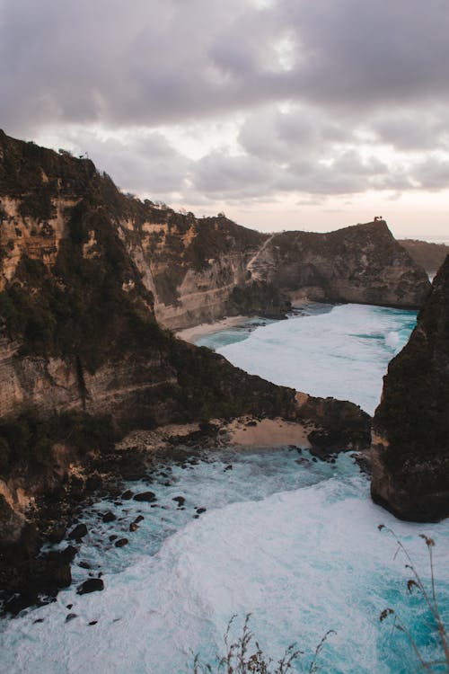 Rocky formation covered by moss and washed by foamy ocean under cloudy sky