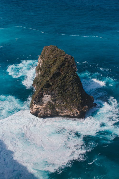 From above of rough stony cliff in foamy blue water of endless deep ocean