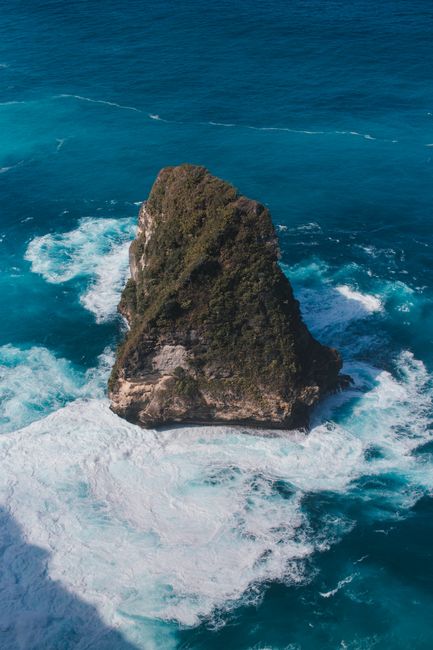 From above of rough stony cliff in foamy blue water of endless deep ocean