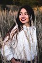 Young smiling female in warm outfit standing in center of dry grass field in sunny autumn evening and looking away